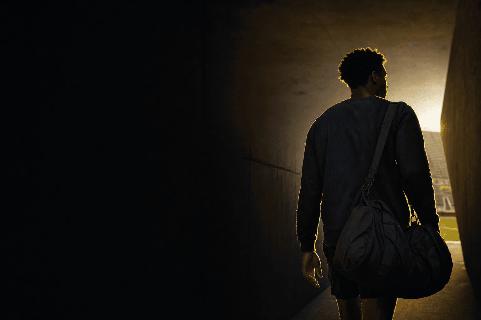 A student-athlete walking out of a stadium tunnel toward the light